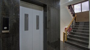 Un ascenseur doté d’un panneau de commande, un escalier avec des rampes en bois et une fenêtre avec des stores.