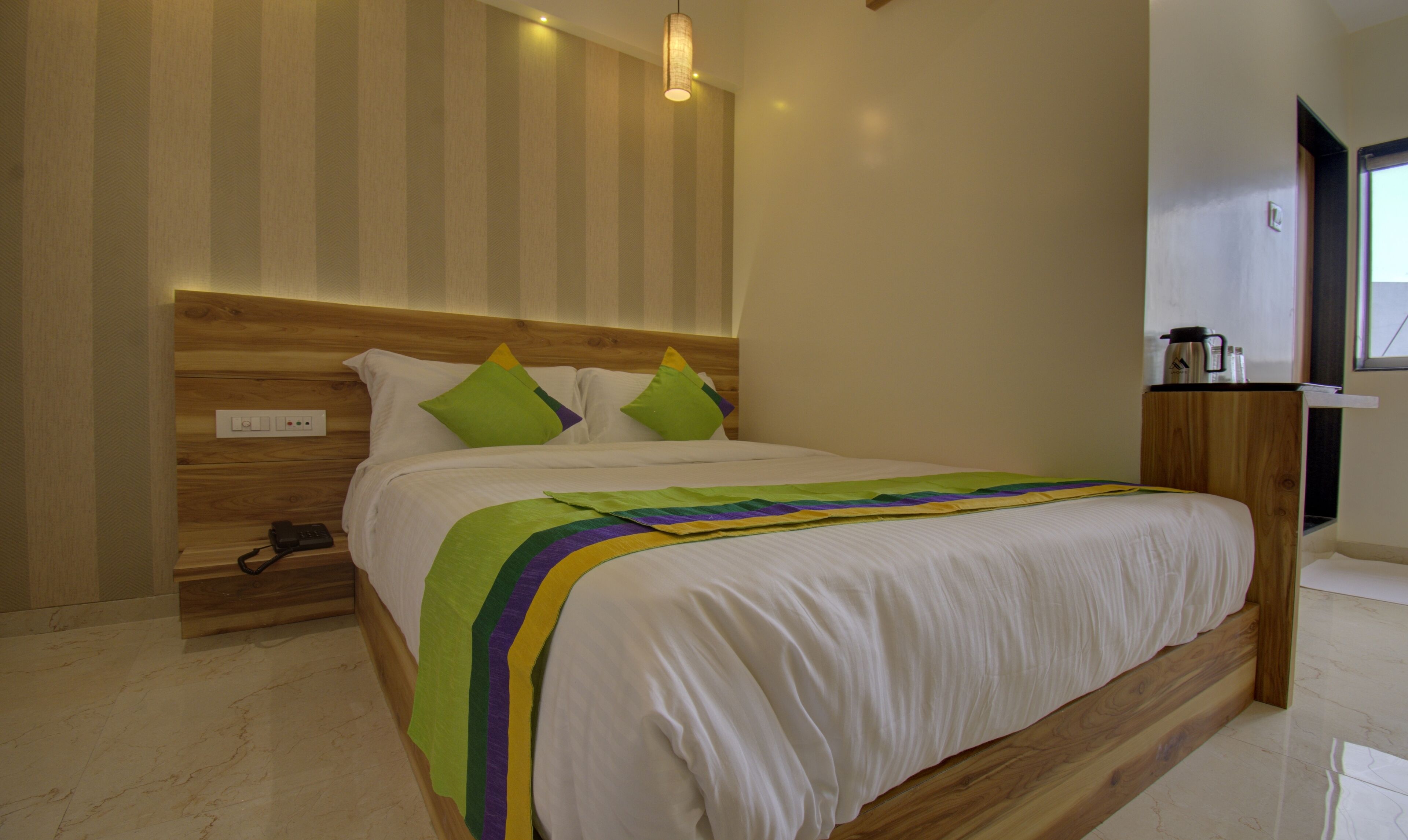A neatly made bed with a white and green striped blanket, a wooden headboard, and a bedside table with a phone and a lamp.