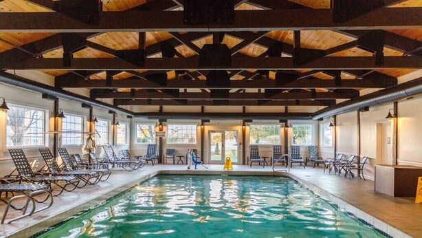 An indoor swimming pool with wooden beams, lounge chairs, and large windows. - Lincoln NH | Ski Retreat | Pool, Near Loon & Hiking Trails (Lincoln)