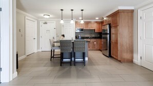 A modern kitchen with wooden cabinets, a built-in oven, and a refrigerator. There is a dining area with two chairs and a table. - Lincoln NH | Ski Retreat | Pool, Near Loon & Hiking Trails (Lincoln)