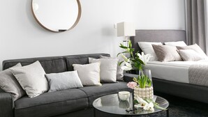 A modern hotel room with a grey sofa, a round mirror, a bedside table with a vase of flowers, and a bed with grey bedding. - Sodispar Szpitalna Old Town Apartments (Kraków)