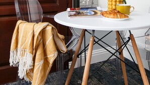 A round table with a white tablecloth, a yellow mug, a plate with food, and a yellow bowl with a plant. A chair with a yellow and white striped blanket is next to the table. - Sodispar Szpitalna Old Town Apartments (Kraków)
