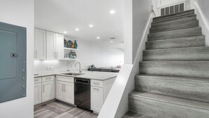 A modern kitchen with white cabinetry, a built-in dishwasher, and a grey staircase leading to an upper level. - Into the Blue - Oceanfront Condo with Beach Access & Gulf Views (Miramar Beach)
