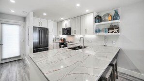 A modern kitchen with white cabinets, a stainless steel refrigerator, a microwave, and a marble countertop. - Into the Blue - Oceanfront Condo with Beach Access & Gulf Views (Miramar Beach)