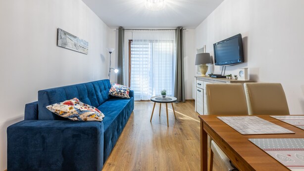 Una sala de estar moderna con un sofá azul, una mesa de comedor de madera y un televisor.
