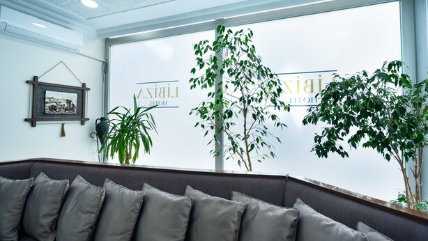 Zona de recepción de un hotel con un ventanal grande, un mostrador de recepción y un área de estar con cojines grises.