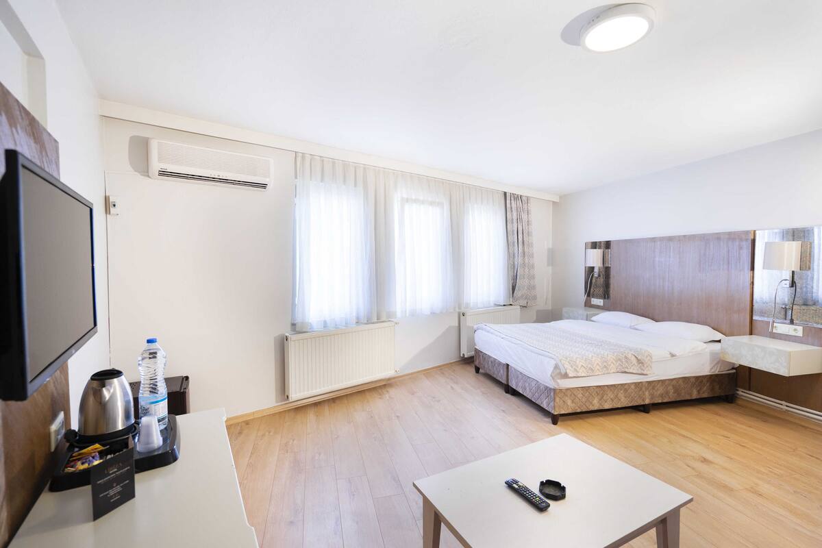 A hotel room with a bed, bedside table, TV, and a small table with a remote control.