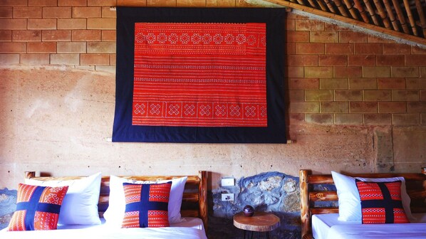 A room with a brick wall, a red patterned tapestry, and wooden furniture with patterned pillows.