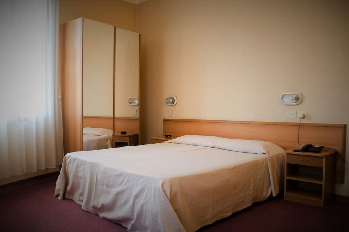 A hotel room with a single bed, a wardrobe, bedside tables, and a mirror.