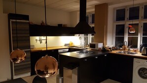 Et moderne køkken med en central ø, rustfrie stålgadgetter og hængende lamper.