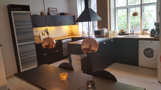 Et moderne køkken med mørke skabe, en central ø, en vaskemaskine og et spiseområde med bord og stole.