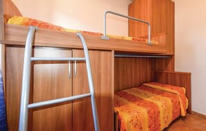 A bunk bed with a ladder, wooden wardrobe, and a bed with a floral bedspread.