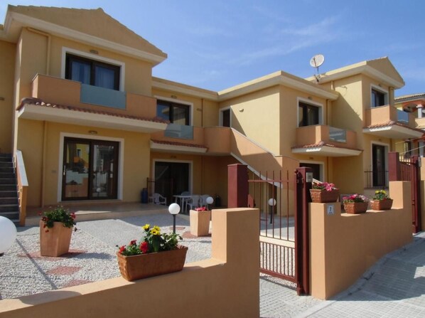 A multi-story residential building with balconies, a gated entrance, and outdoor seating.