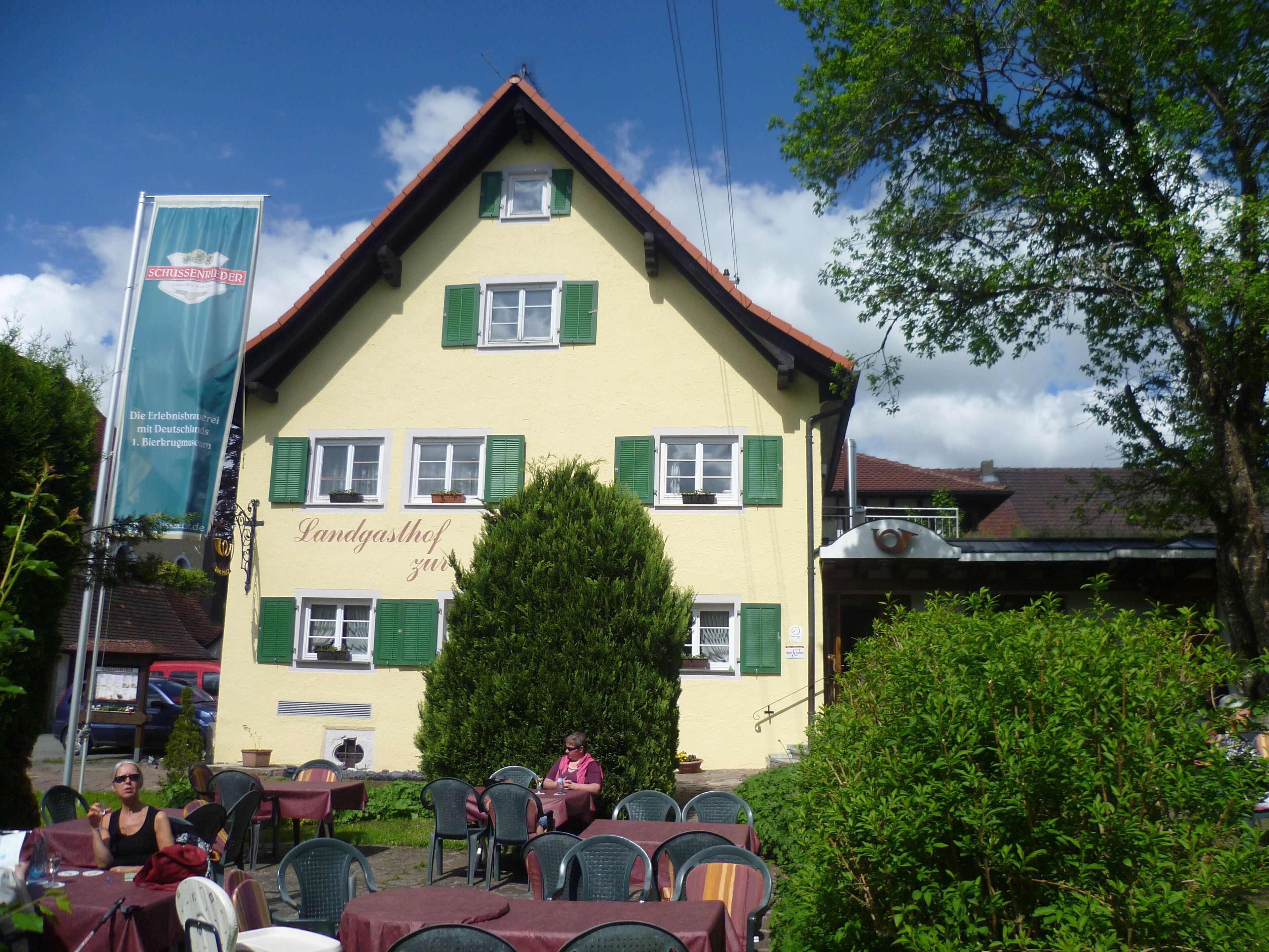 A building with a yellow facade and green shutters, featuring outdoor seating with tables and chairs.