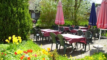 An outdoor patio with tables and chairs, surrounded by greenery and flowers.