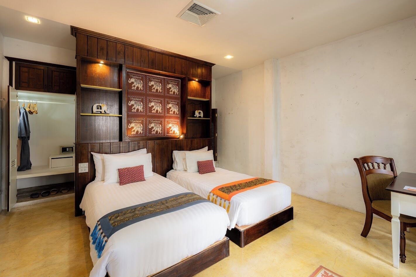 A hotel room with two beds, wooden headboard, a desk, and a chair.