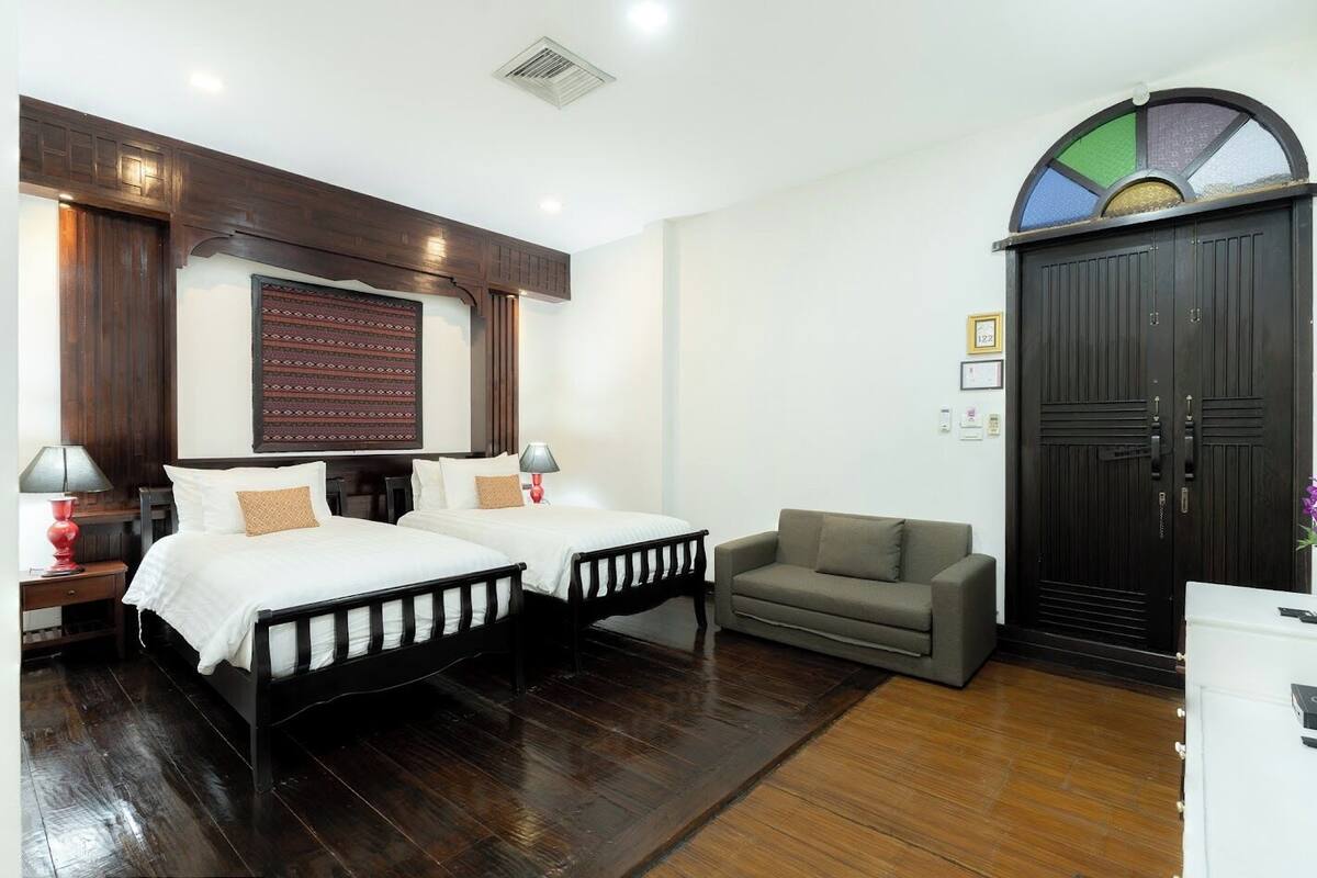 Habitación de hotel con dos camas, un sofá, una puerta grande de madera y una obra de arte colgada en la pared.