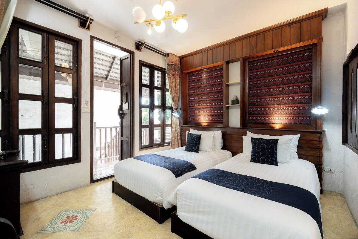 Habitación con dos camas, cabecero de madera, balcón y pared decorada.