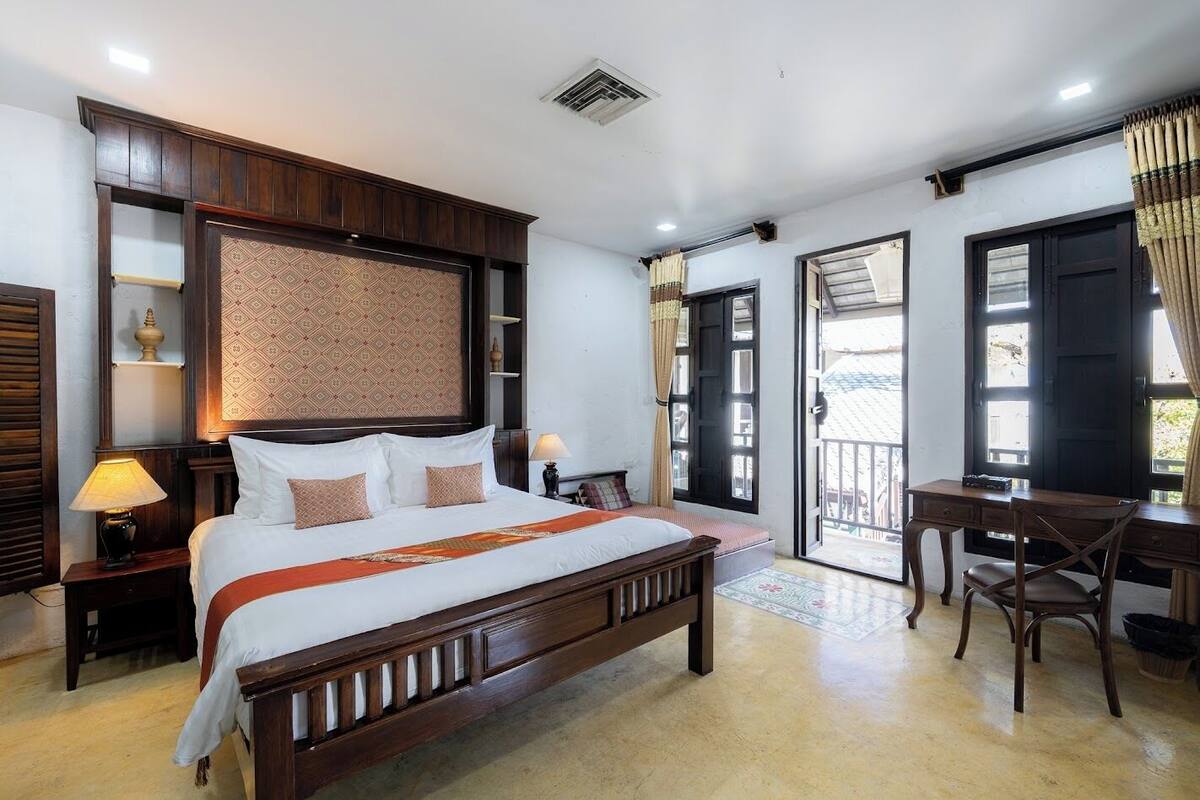 Un dormitorio con una cama grande, un escritorio y una silla. Hay una ventana con cortinas y una puerta que da a un espacio al aire libre.