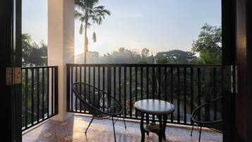 A balcony with two chairs and a table, a patterned floor, and a view of palm trees and greenery.