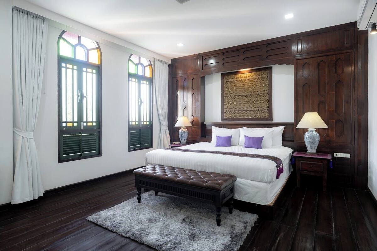 Un dormitorio con una cama grande, dos lámparas de noche, un cabecero de madera, un panel decorativo en la pared y una ventana con contraventanas.
