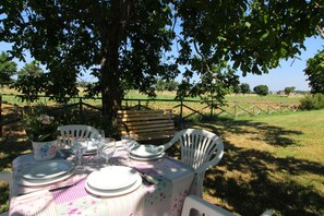 Enjoy al fresco dining in a serene countryside setting with a table for four, surrounded by a wooden bench and lush greenery.