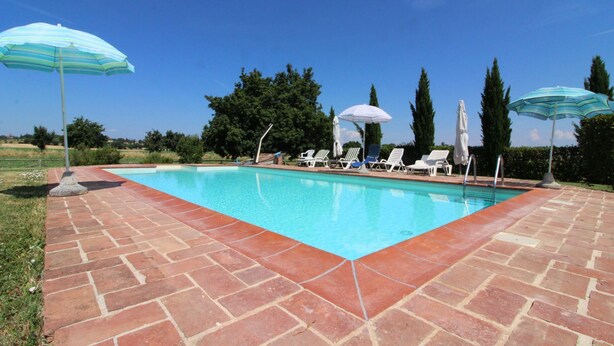 A rectangular swimming pool with a brick border, surrounded by lounge chairs and umbrellas. - Il Viaggiolo (Foiano della Chiana)