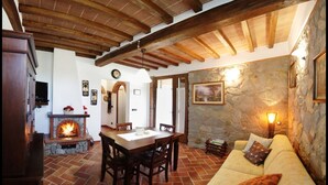 A cozy living room with a stone wall, a fireplace, a dining area with a table and chairs, and a sofa with cushions. - La Casetta nel Bosco (Sinalunga)