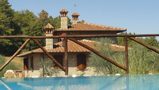 A stone villa with a tiled roof, a swimming pool, and a rustic metal fence. - La Casetta nel Bosco (Sinalunga)