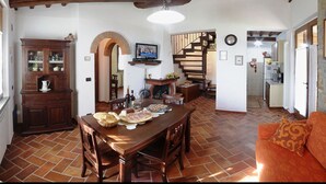 A spacious living area with a wooden dining table, a sofa, and a kitchen in the background. - La Casetta nel Bosco (Sinalunga)