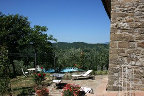 Um pátio com móveis de exterior, um muro de pedra e vista para uma colina arborizada.