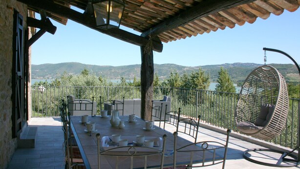 A terrace with a table set for tea, a hanging chair, and a view of the hills. - Monte del Lago (Magione)