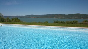 A swimming pool with clear blue water, surrounded by greenery and a view of a lake and distant hills. - Monte del Lago (Magione)