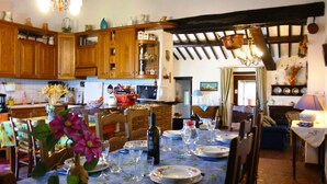 A traditional kitchen with wooden cabinets, a dining table set for four, and a stone fireplace. - Monte del Lago (Magione)