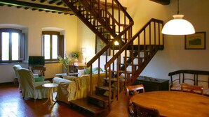 A cozy living room with a wooden staircase, a dining table, and comfortable seating. - Olivo (Arezzo)