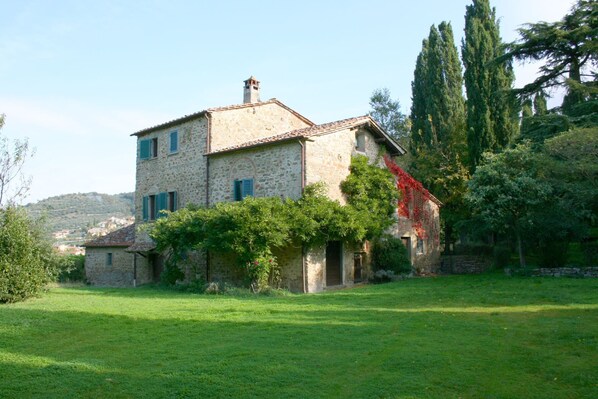 A stone house with a tiled roof, surrounded by a grassy yard and trees.