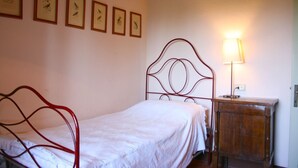 A bedroom with a metal bed frame, a bedside table, a lamp, and framed pictures on the wall. - Olivo (Arezzo)