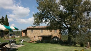A stone building with a tiled roof, surrounded by a well-maintained lawn and a large tree.