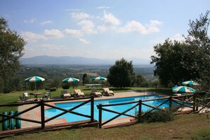A pool with a wooden fence, lounge chairs, and umbrellas. - Podere della Crocchia (Civitella in Val di Chiana)