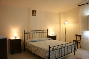 A bedroom with a bed, two bedside tables, a nightstand, a chair, a floor lamp, and a wall-mounted picture. - Poggio Falcone (Castiglione del Lago)