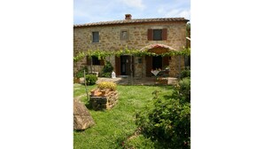 A stone building with a tiled roof, a garden with various plants, and a small table with a tablecloth. - San Eusebio (Cortona)