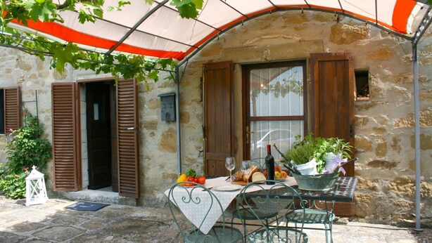 An outdoor dining area with a table set for two, surrounded by stone walls and wooden shutters. - San Eusebio (Cortona)