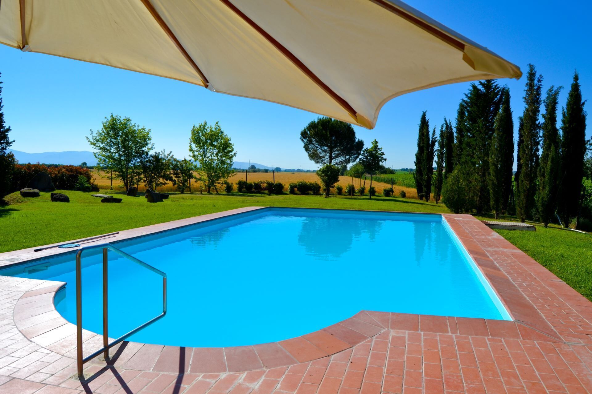 Une piscine avec une terrasse en briques et un auvent.