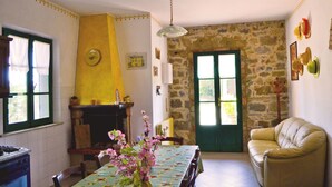 A cozy living room with a fireplace, a dining table with a floral tablecloth, a sofa, and a stone wall. - Villa Cantagallo (Cortona)