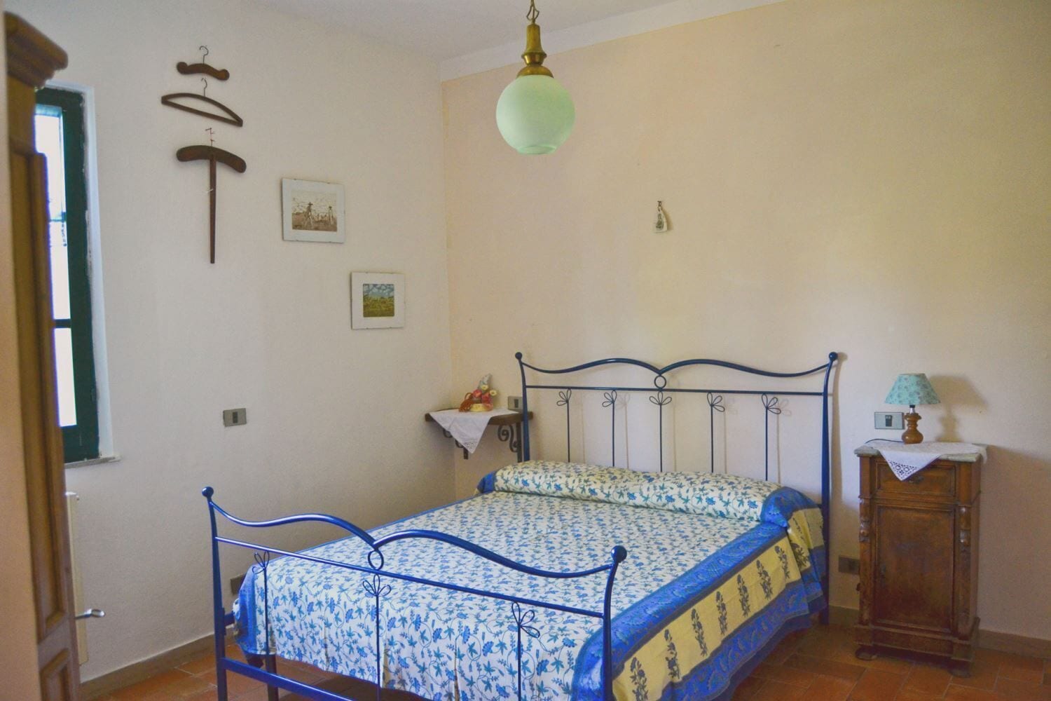 Une chambre à coucher comprenant un lit, une commode, un luminaire suspendu et deux cadres photos fixés au mur.