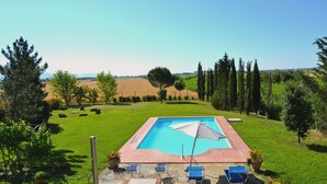 A rectangular swimming pool with a tiled deck, surrounded by a grassy lawn and trees. - Villa Cantagallo (Cortona)