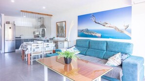A modern living room with a blue sofa, a glass coffee table, and a dining area with a white table and chairs. - Apartment near beach and nightlife, perfect for fun holidays (Alc údia)