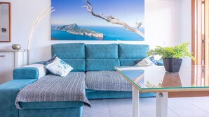 A modern living room with a teal sofa, a glass coffee table, and a large landscape painting of a coastal scene. - Apartment near beach and nightlife, perfect for fun holidays (Alcúdia)