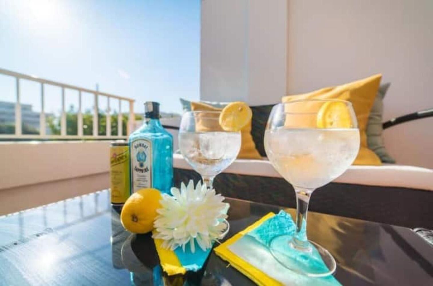 A balcony with a table set for drinks, a bottle of liquor, and a flower arrangement.