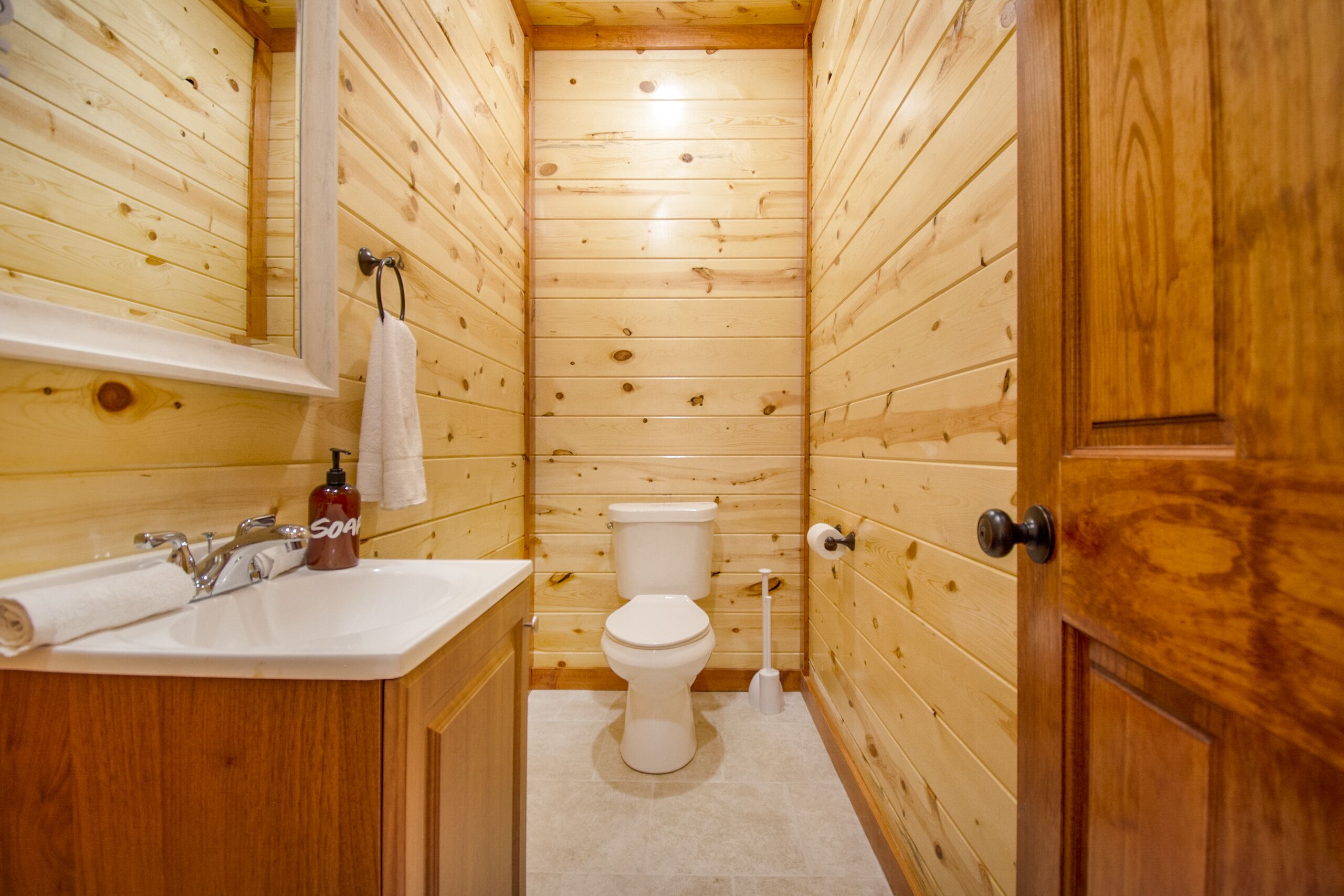 A wooden-paneled bathroom with a sink, toilet, and mirror.